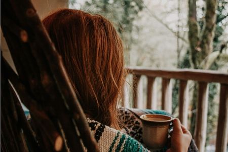 Woman on veranda holding a hot drink, looking out and feeling contemplative