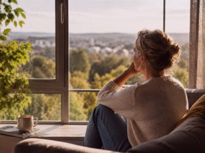 A woman looking out of an upper floor window at the landscape below and ahead, contemplating late ADHD diagnosis